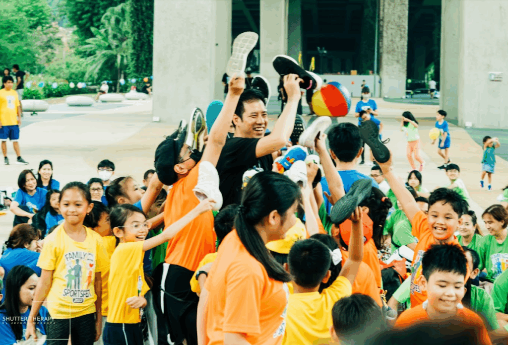 A group of students at a family sportsfest event with their teacher, holding up their shoes.